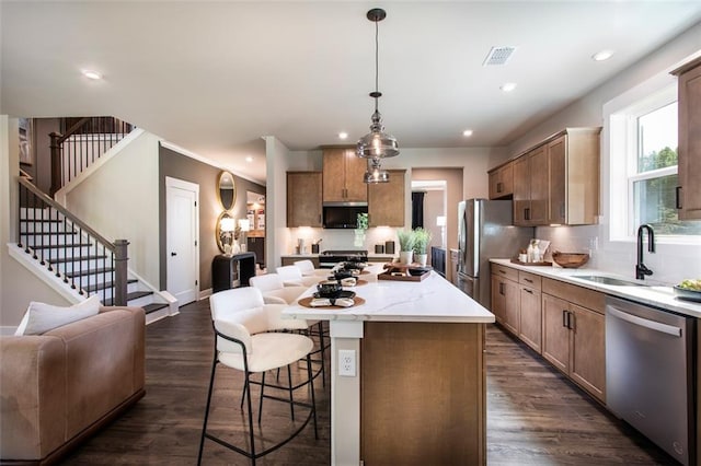 kitchen featuring sink, a kitchen island, decorative light fixtures, appliances with stainless steel finishes, and dark hardwood / wood-style flooring