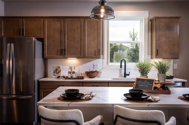 kitchen with sink, decorative light fixtures, stainless steel fridge with ice dispenser, a breakfast bar, and decorative backsplash