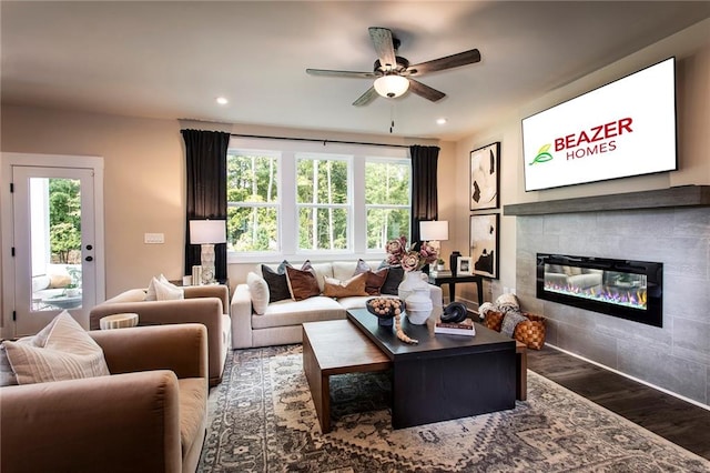 living room featuring wood-type flooring, ceiling fan, and a tile fireplace