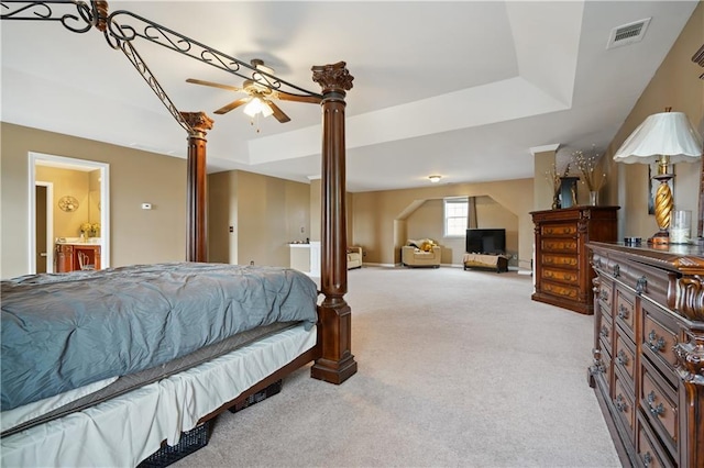 carpeted bedroom with connected bathroom, decorative columns, a tray ceiling, and ceiling fan