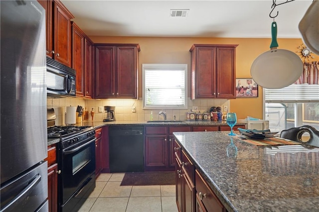 kitchen with light tile patterned flooring, sink, black appliances, dark stone countertops, and decorative backsplash