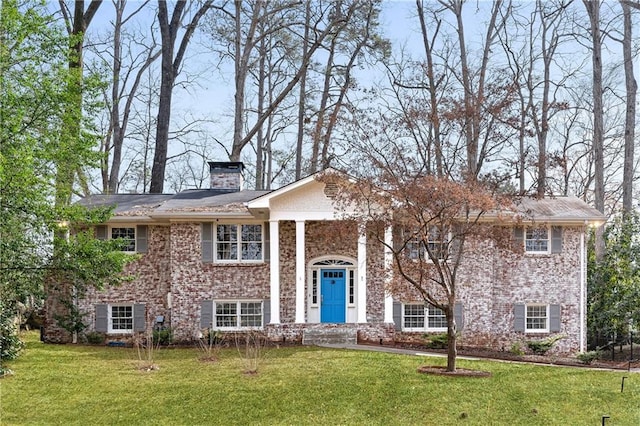 view of front of home featuring brick siding, a chimney, and a front yard