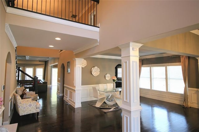 interior space featuring decorative columns, ornamental molding, dark hardwood / wood-style floors, and a high ceiling