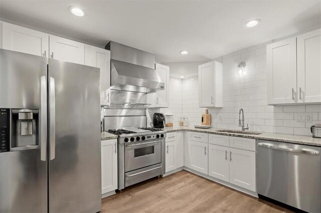 kitchen with wall chimney range hood, sink, stainless steel appliances, light stone countertops, and white cabinetry