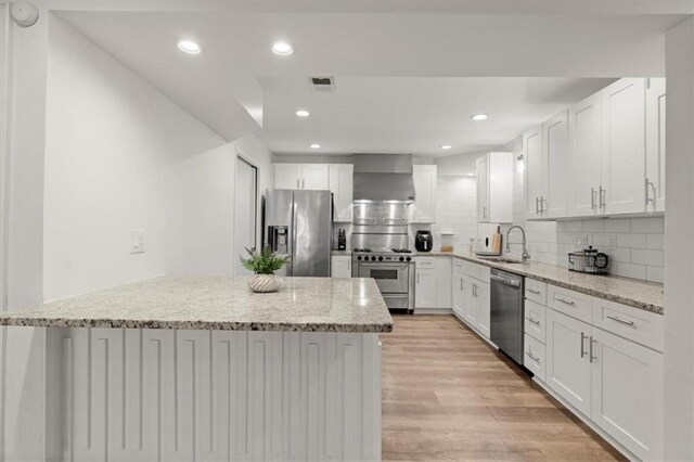 kitchen featuring stainless steel appliances, light stone countertops, white cabinets, and wall chimney exhaust hood