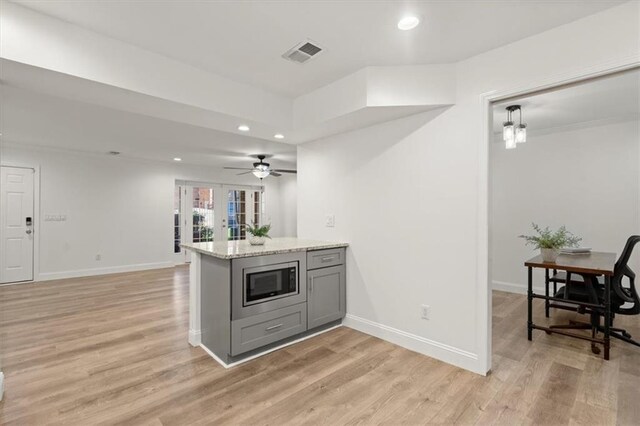 kitchen featuring decorative light fixtures, light hardwood / wood-style flooring, gray cabinets, light stone countertops, and stainless steel microwave