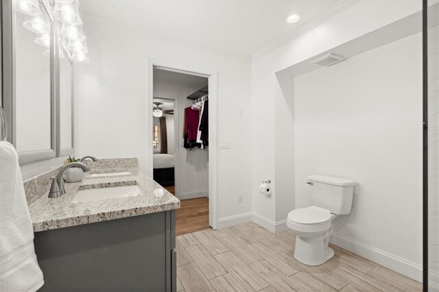 bathroom featuring ceiling fan, vanity, wood-type flooring, crown molding, and toilet