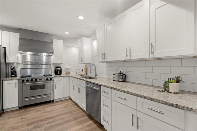 kitchen with light wood-type flooring, sink, wall chimney range hood, white cabinetry, and appliances with stainless steel finishes