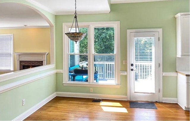 doorway to outside featuring crown molding, a fireplace, baseboards, and wood finished floors