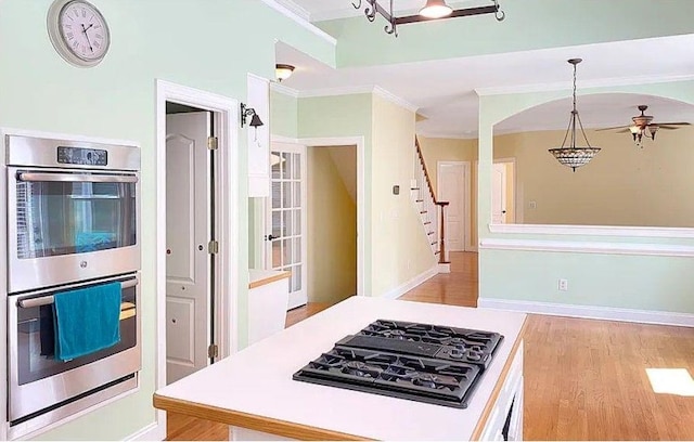 kitchen with double oven, black gas stovetop, hanging light fixtures, light wood finished floors, and crown molding