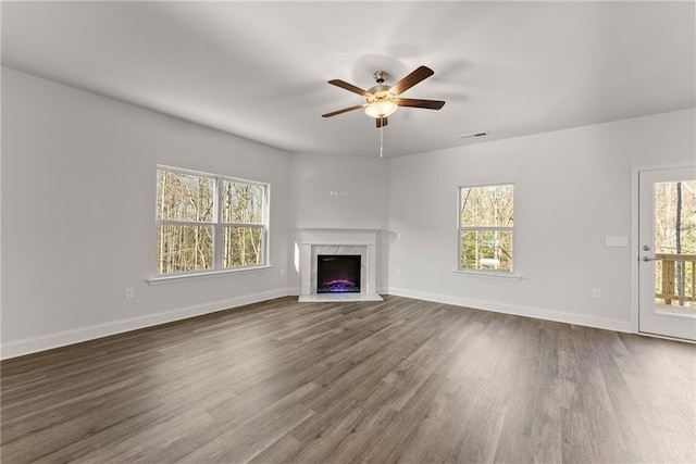 unfurnished living room featuring dark wood-style floors, a fireplace, a ceiling fan, and plenty of natural light