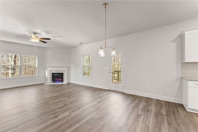 unfurnished living room with baseboards, a fireplace, ceiling fan, and wood finished floors
