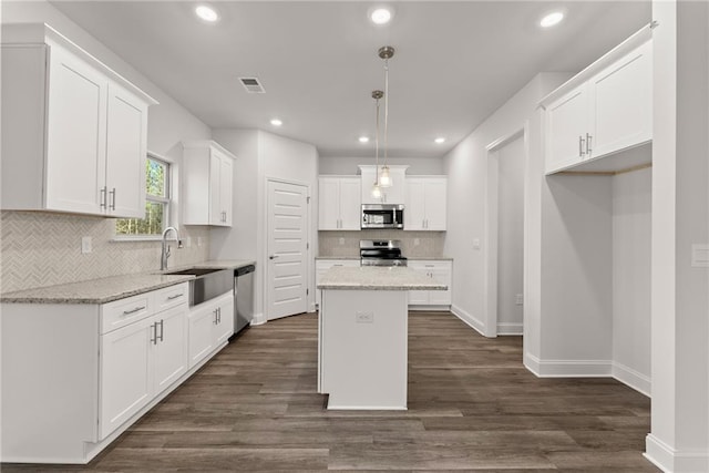 kitchen with visible vents, a sink, a kitchen island, stainless steel appliances, and white cabinets