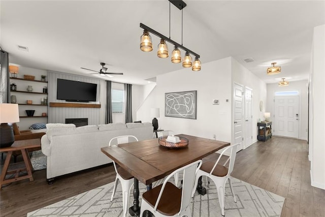 dining room featuring visible vents, ceiling fan, a fireplace, and wood finished floors