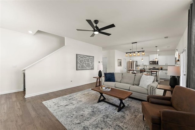 living room with dark wood-style floors, visible vents, ceiling fan, and baseboards