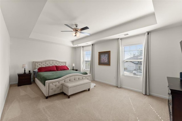 bedroom with multiple windows, a raised ceiling, light colored carpet, and baseboards