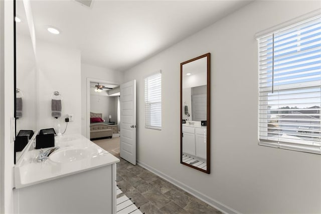 ensuite bathroom featuring double vanity, connected bathroom, baseboards, and a sink