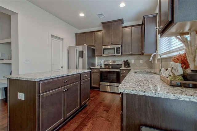 kitchen featuring sink, dark wood-type flooring, light stone counters, a kitchen island, and appliances with stainless steel finishes