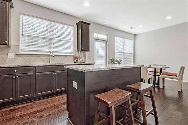 kitchen featuring light stone countertops, dark hardwood / wood-style flooring, dark brown cabinetry, sink, and a center island