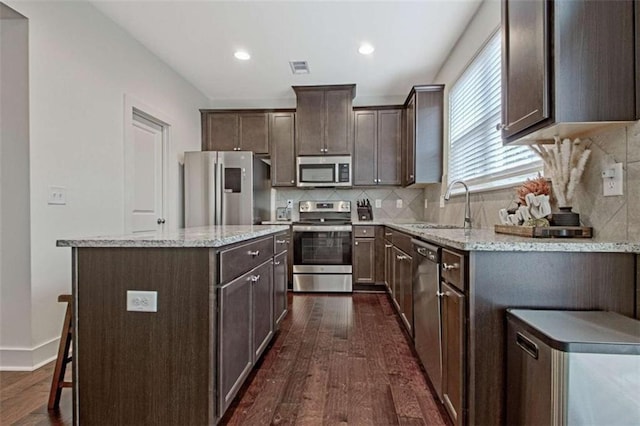 kitchen featuring a center island, dark wood-type flooring, sink, light stone counters, and stainless steel appliances