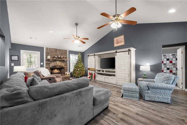 living room featuring hardwood / wood-style flooring, vaulted ceiling, a barn door, a fireplace, and ceiling fan