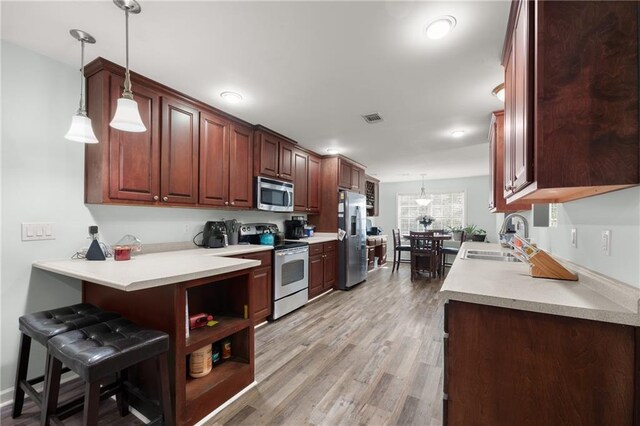 kitchen with appliances with stainless steel finishes, pendant lighting, kitchen peninsula, and sink