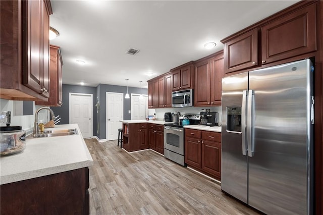 kitchen featuring appliances with stainless steel finishes, light hardwood / wood-style floors, decorative light fixtures, and sink