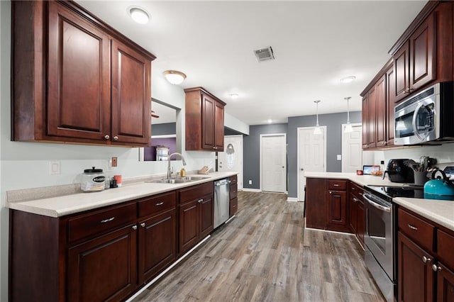 kitchen featuring decorative light fixtures, appliances with stainless steel finishes, light hardwood / wood-style flooring, and sink