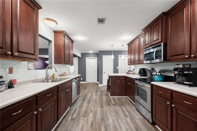 kitchen featuring sink, stainless steel appliances, light hardwood / wood-style floors, and hanging light fixtures