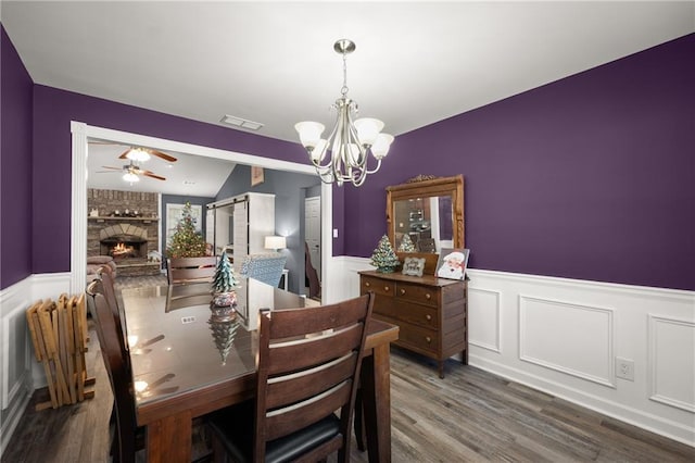 dining room featuring lofted ceiling, a brick fireplace, ceiling fan with notable chandelier, and hardwood / wood-style floors