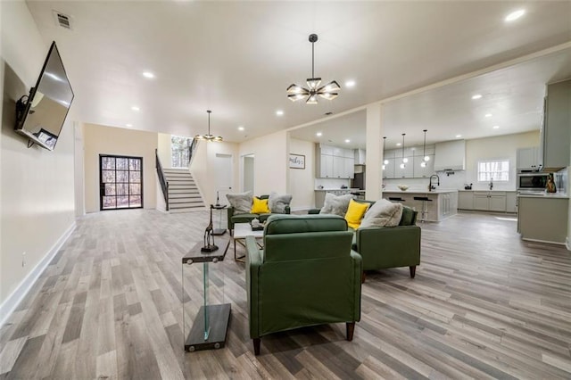 living room with an inviting chandelier, sink, and light hardwood / wood-style flooring