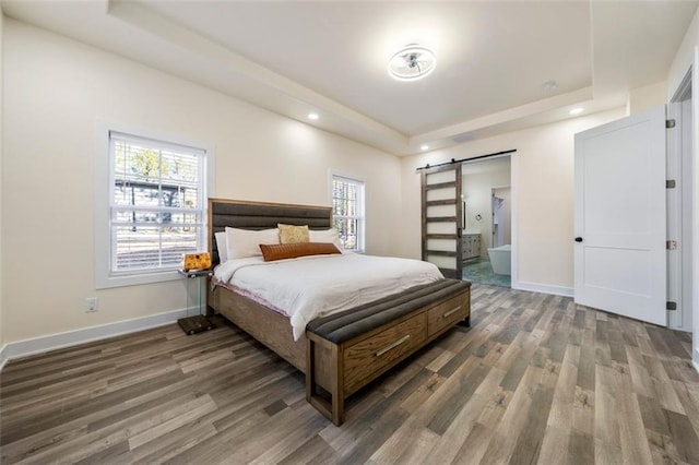 bedroom with a barn door, dark wood-type flooring, and a tray ceiling