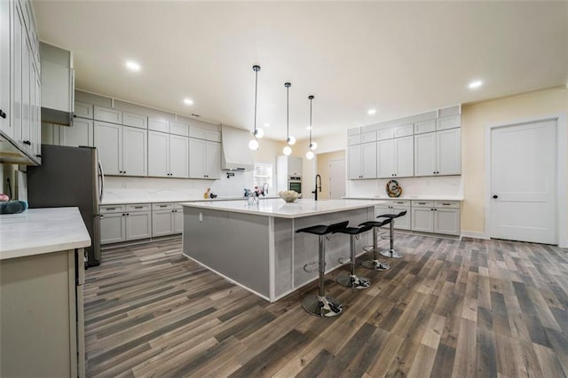 kitchen featuring a kitchen breakfast bar, hanging light fixtures, a kitchen island with sink, stainless steel appliances, and dark wood-type flooring