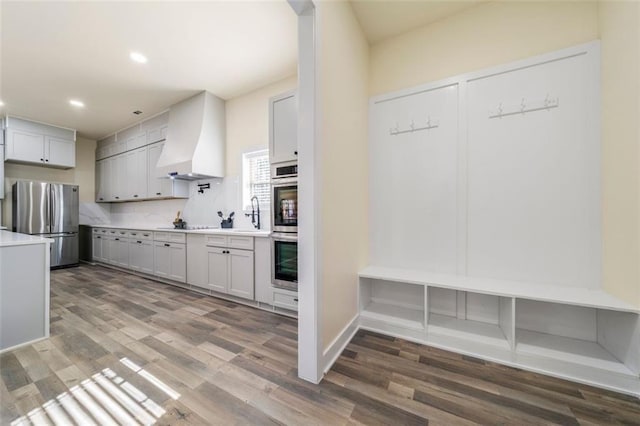 kitchen featuring hardwood / wood-style flooring, appliances with stainless steel finishes, decorative backsplash, and wall chimney range hood