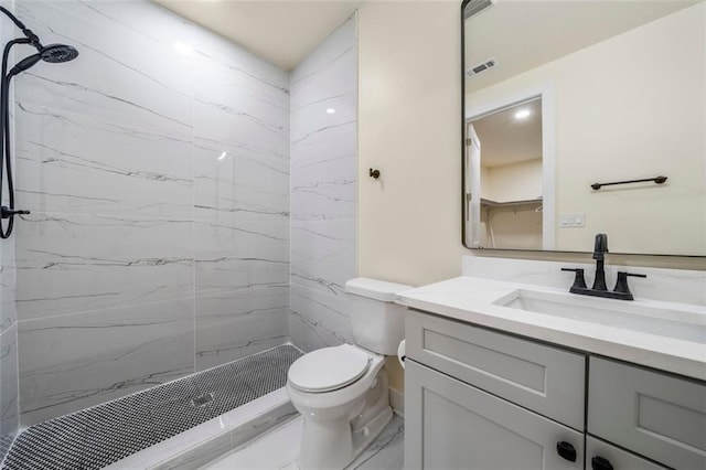 bathroom featuring vanity, a tile shower, and toilet