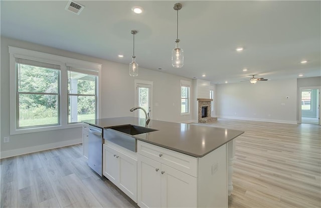 kitchen with a center island with sink, decorative light fixtures, stainless steel dishwasher, white cabinets, and sink