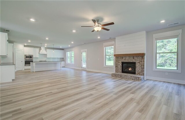 unfurnished living room with ceiling fan, a brick fireplace, and light hardwood / wood-style floors