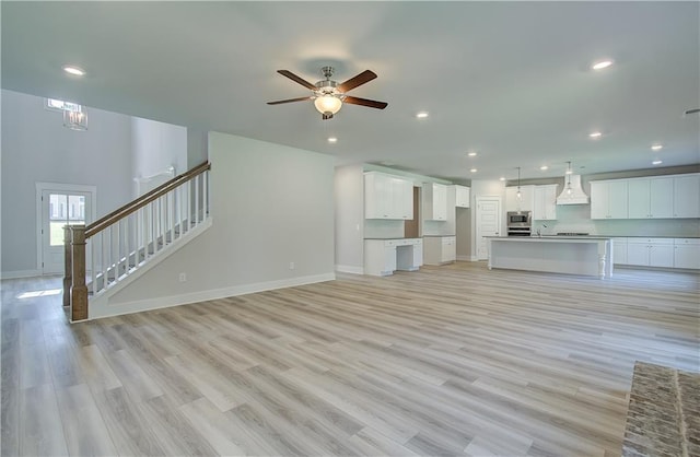 unfurnished living room with light hardwood / wood-style floors, sink, and ceiling fan with notable chandelier