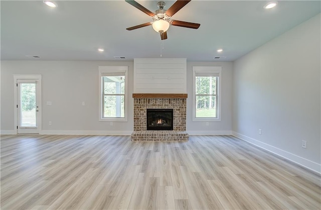 unfurnished living room with ceiling fan, a brick fireplace, a wealth of natural light, and light hardwood / wood-style floors