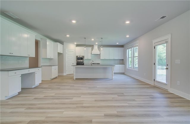 kitchen featuring a kitchen island with sink, white cabinets, and custom range hood