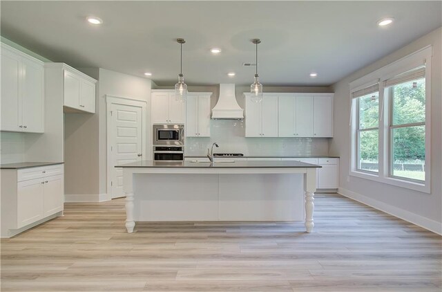 kitchen featuring decorative light fixtures, a center island with sink, custom exhaust hood, white cabinetry, and stainless steel appliances