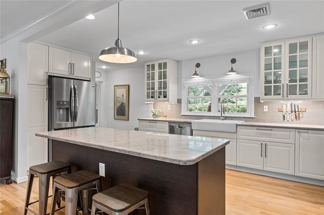 kitchen with stainless steel appliances, a sink, a breakfast bar area, light wood-style floors, and white cabinets