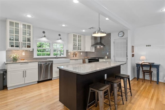 kitchen with stainless steel appliances, wall chimney exhaust hood, a sink, white cabinetry, and recessed lighting