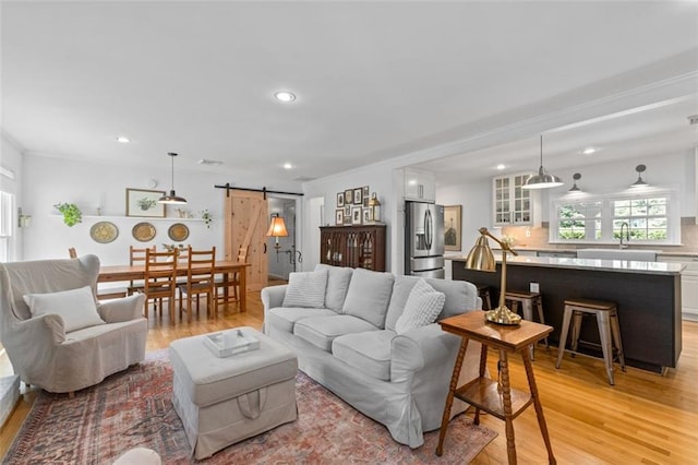 living room featuring a barn door, light wood-type flooring, healthy amount of natural light, recessed lighting, and crown molding