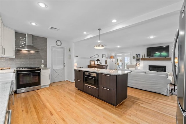 kitchen featuring stainless steel appliances, wall chimney range hood, a fireplace, white cabinets, and recessed lighting