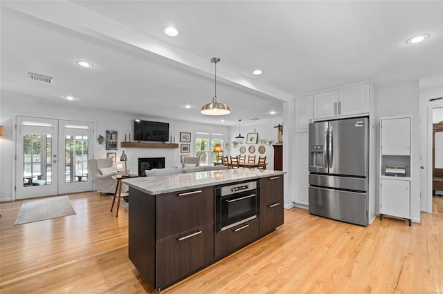 kitchen with stainless steel appliances, dark brown cabinets, a brick fireplace, light wood-style flooring, and decorative light fixtures