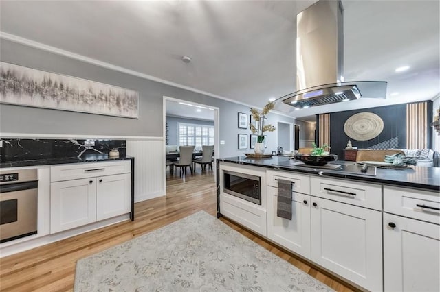 kitchen with white cabinetry, light wood-type flooring, appliances with stainless steel finishes, ornamental molding, and island range hood