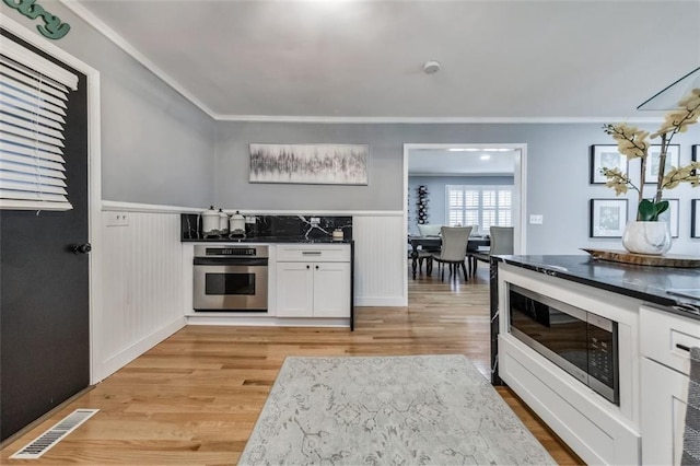 kitchen with light hardwood / wood-style floors, white cabinetry, appliances with stainless steel finishes, and ornamental molding