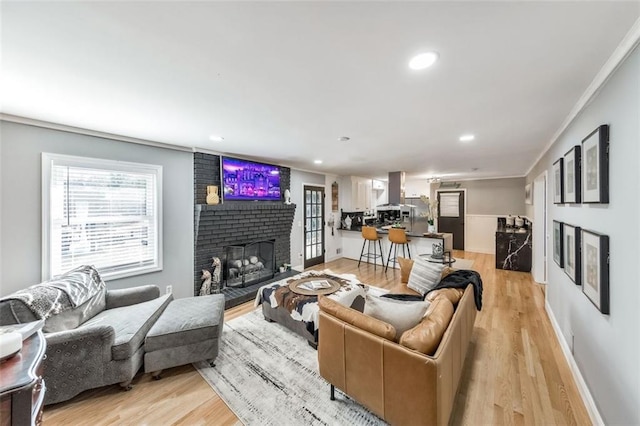 living room featuring light wood-type flooring, crown molding, and a fireplace