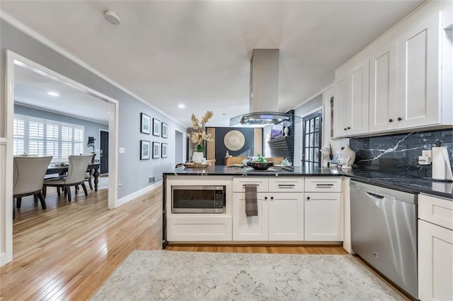 kitchen featuring island exhaust hood, appliances with stainless steel finishes, decorative backsplash, and white cabinetry